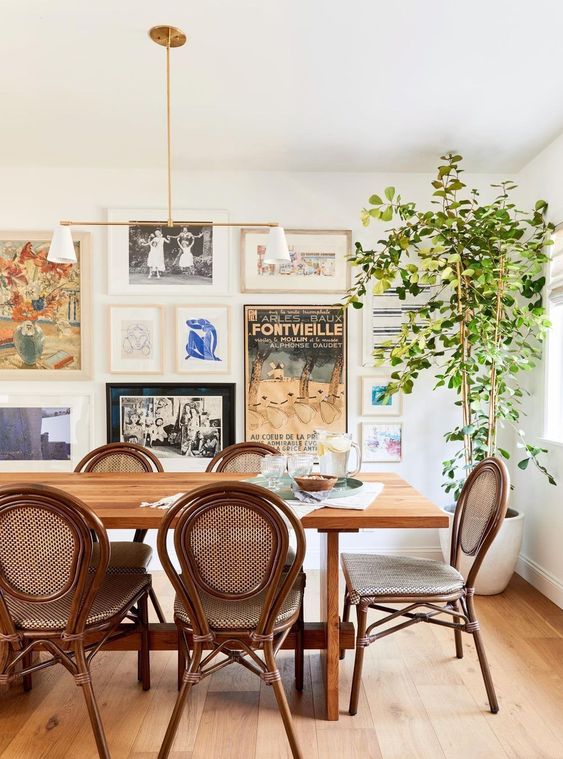 a beautiful eclectic dining room with a stained table and vintage chairs, a potted tree and a free form gallery wall with much color