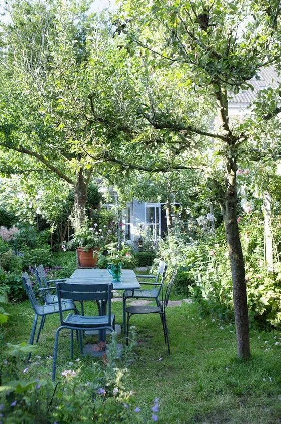 a beautiful garden dining zone with blue metal furniture and greenery and blooms plus trees around is chic