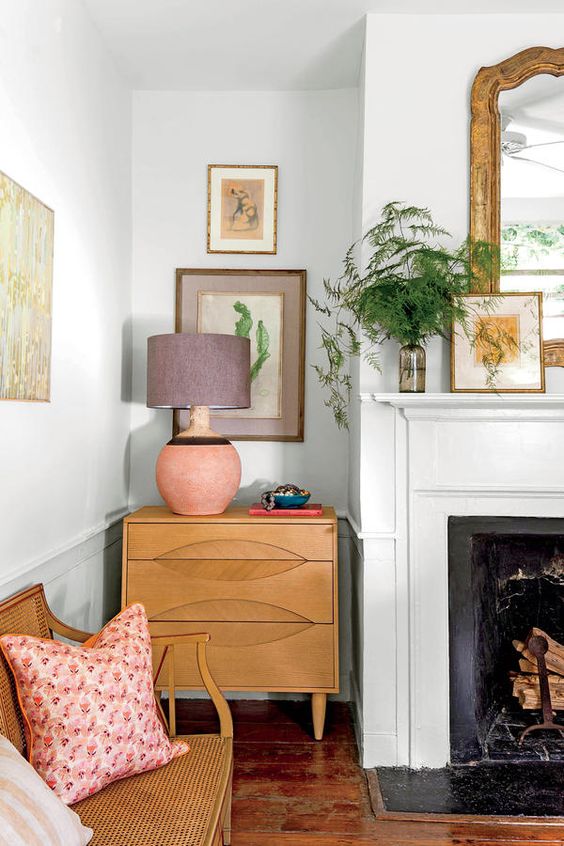 a beautiful living room with a fireplace, a rattan bench with pillows, a dresser, a mini gallery wall and some more art around