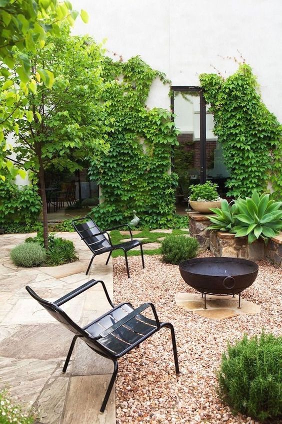 a beautiful modern backyard with a black metal fire bowl and black metal chairs plus lots of greenery around