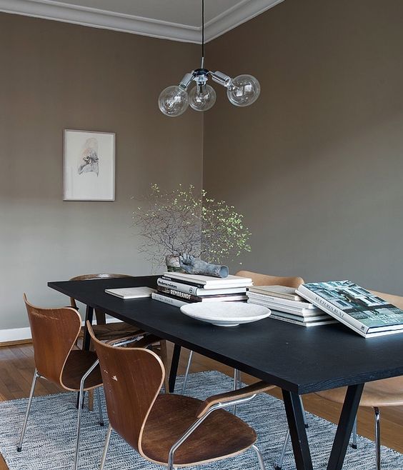 a beautiful taupe Scandinavian dining room with a black table and cool and timeless chairs, some books and art