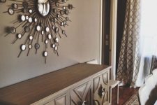 a beautiful taupe dining room with a gorgeous sunburst mirror, a credenza, a dining table and chairs, printed curtains and a ceiling