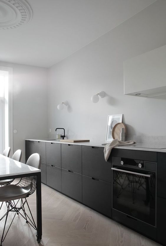 a black and white kitchen with no hardware cabinets, a white hood, a white table and neutral chairs and black fixtures is cool