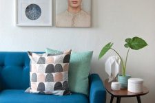 a blue mid-century modern sofa, a side table with gilded legs and a mini gallery wall with a meaning