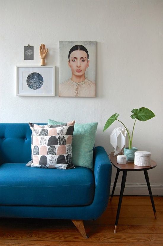 a blue mid-century modern sofa, a side table with gilded legs and a mini gallery wall with a meaning