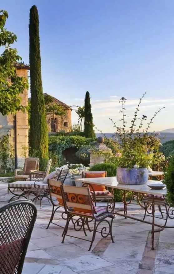 a bold Provence terrace with vintage forged furniture, a table with a stone tabletop, greenery and blooms and striped textiles