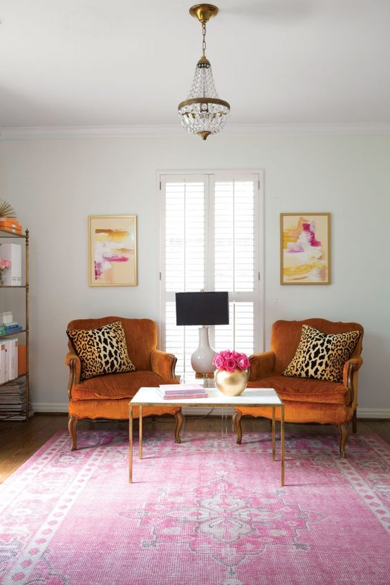 a bright and chic space with rust-colored vintage chairs, a pink printed rug, a storage unit and bold artworks