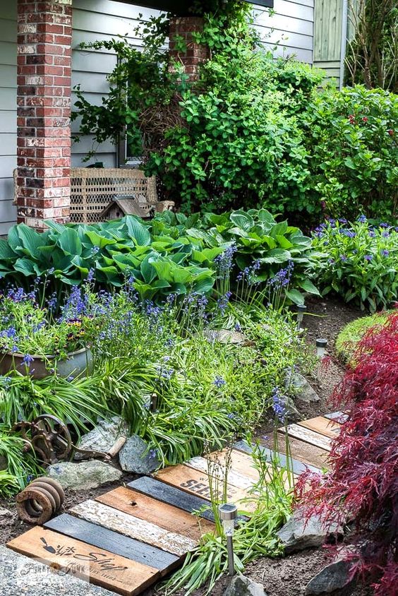 a lovely small garden design a bright floral garden with lots of greenery and colorful foliage, a reclaimed wooden walkway adds a lovely relaxed and rustic feel to the space