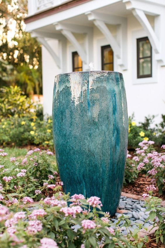 a bright front yard with blooms and greenery plus pebbles and a blue planter fountain is low maintenance and chic