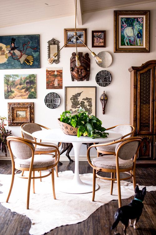 a catchy dining room with a round table and vintage chairs, a rug, a free form gallery wall and a cool chandelier