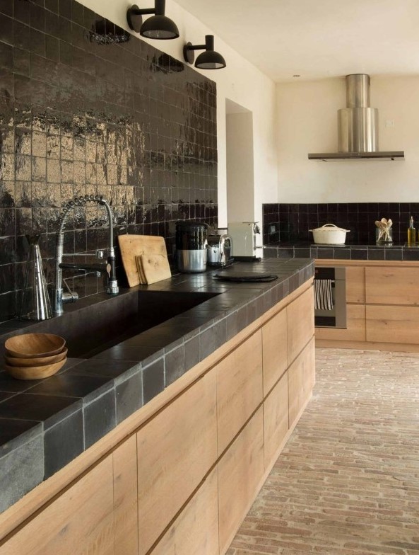 a catchy eclectic kitchen with sleek blonde wood cabinets, black tiles on the backsplash and countertops, black sonces