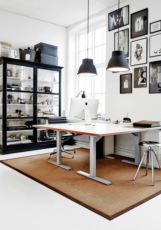 a chic Scandinavian home office with a shared desk, a large glass storage unit, a gallery wall in black and white and black pendant lamps