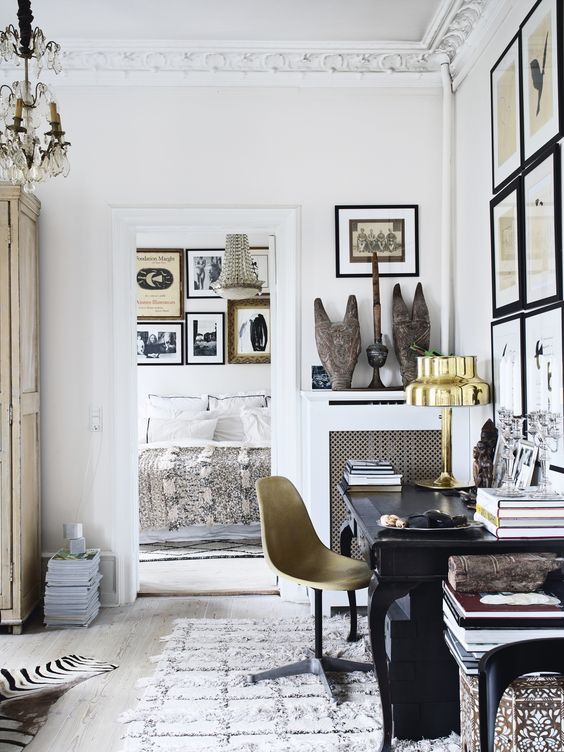a chic and refined home office with a black vintage desk, a gold chair and a gold table lamp, a largre gallery wall and a chandelier