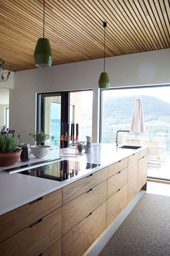 a chic contemporary kitchen done in white and light-stained wood, with no hardware cabinets and a gorgeous lake view plus pendant lamps