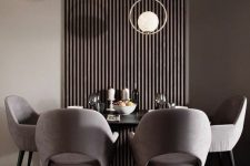 a chic contemporary taupe dining room with a dark wooden slats on the wall, a black table, grey chairs and catchy pendant lamps