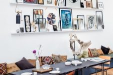 a chic dining room with a boho feel and a bright gallery wall done with white ledges and colorful artworks and decorations that enlivens the space