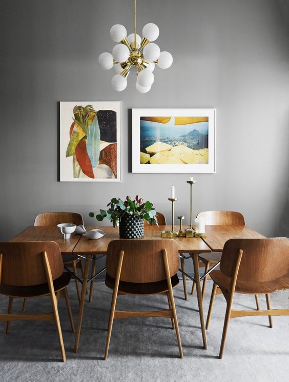 a chic dining room with grey walls, a stained table and chairs, a colorful mini gallery wall and a cool chandelier