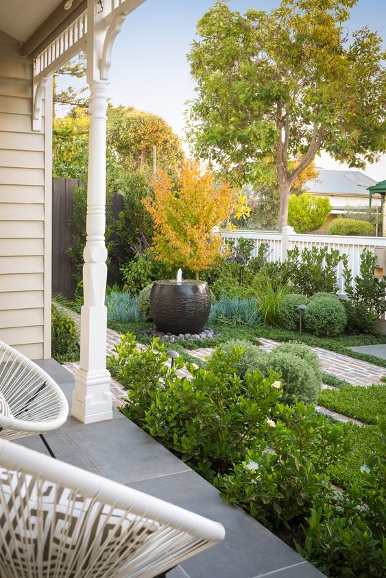 a chic front yard done with greenery, a brick path and a modern black wrought bowl fountain is gorgeous