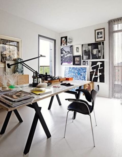 a chic home office with a large black and white desk, a black chair, a stained credenza, a bold gallery wall and a table lamp