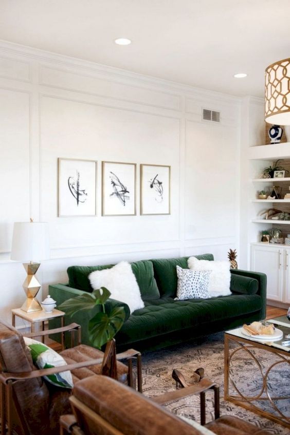 a chic mid-century modenr living room with built-in shelves and cabinets, a green sofa, brown leather chairs, chic tables and a mini gallery wall