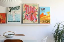 a chic mid-century modern dining room with a white table and timber and metal chairs, a ledge gallery wall with bold posters