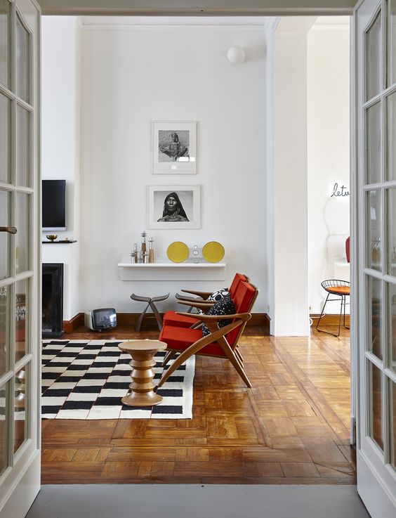 a chic mid-century modern living room with a printed rug, red chairs, side tables and a mini black and white gallery wall
