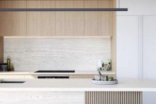 a chic minimalist kitchen done in neutrals, with no hardware cabinets, a stone backsplash and a kitchen island, black fixtures