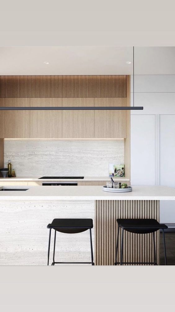 a chic minimalist kitchen done in neutrals, with no hardware cabinets, a stone backsplash and a kitchen island, black fixtures