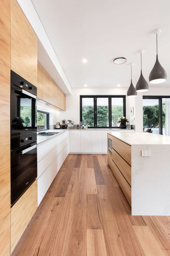 a chic minimalist kitchen with no hardware white cabinets, a sleek kitchen island with a stone countertop, a window backspalash and black lamps
