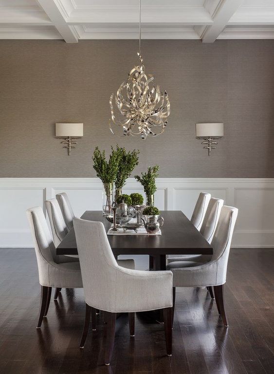 a chic modern dining room with taupe grasscloth wallpaper walls, creamy paneling, a black table and neutral chairs, a lovely chandelier