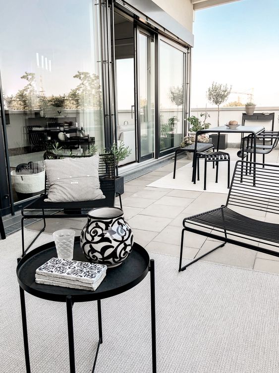 a chic modern terrace done in neutrals and accented with black metal furniture - a table and chairs, loveseats and a round table