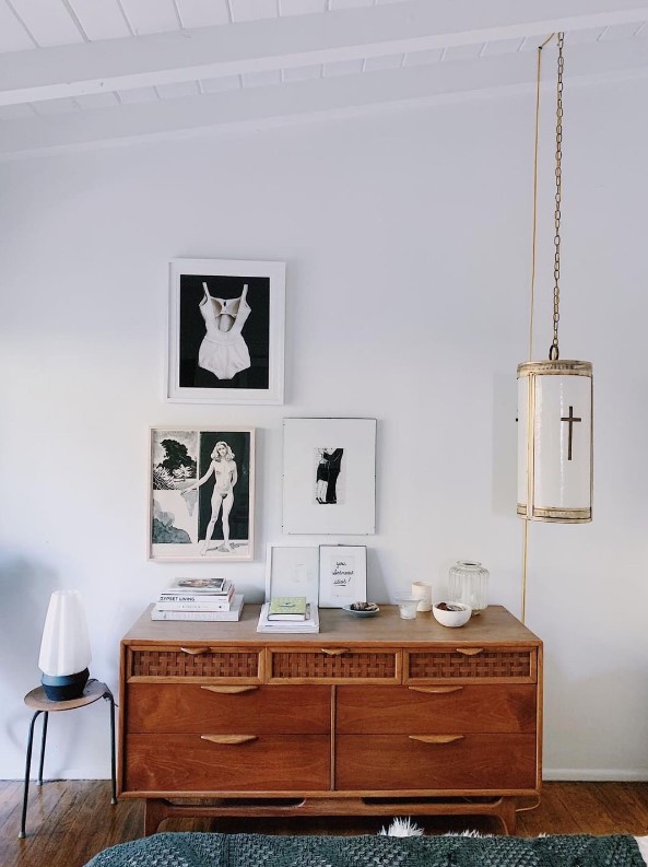 a chic space with a vintage rich-stained credenza, a black and white gallery wall with a refined feel and a catchy pendant lamp on chain