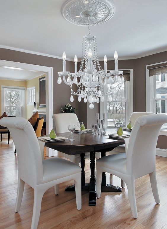 a chic taupe dining room with a dark-stained dining table and creamy chairs, a chic chandelier and a ceiling medallion to accent it