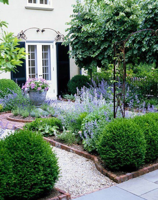 a classic small garden with garden beds lined with bricks and white gravel paths that are manicured and are very neat