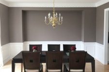 a clean mid-century modern to vintage dining room with creamy paneling, a black table and dark chairs, a gold chandelier