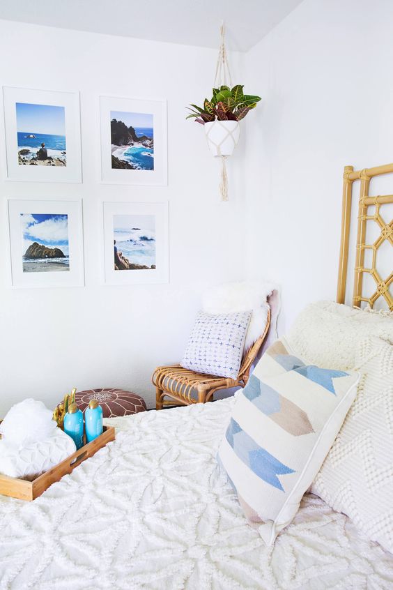 a coastal bedroom with a rattan bed and a chair, a leather pouf, neutral bedding, a bold sea photo gallery wall
