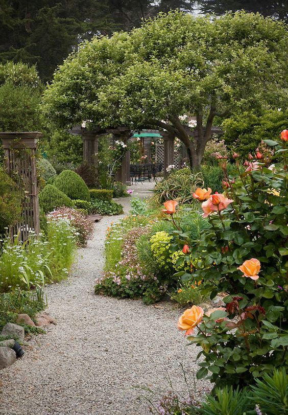 a colorful and bold garden with lots of blooms and trees, with gravel pathways and some wooden furniture