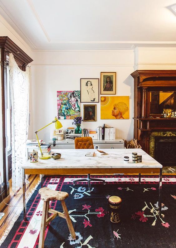 a colorful home office with a marble desk, a leather chair and a wooden stool, a built-in fireplace, a credenza, a colorful gallery wall