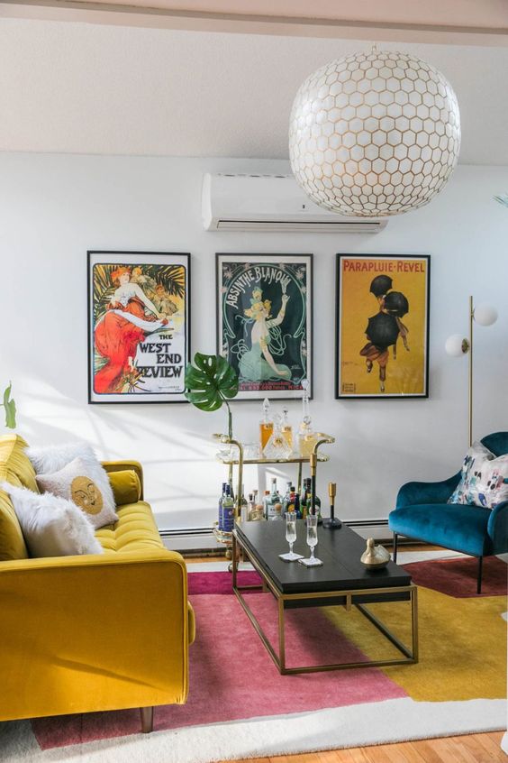 a colorful mid-century modern living room with a mustard sofa, a navy chair, a color block rug and a bright vintage poster gallery wall