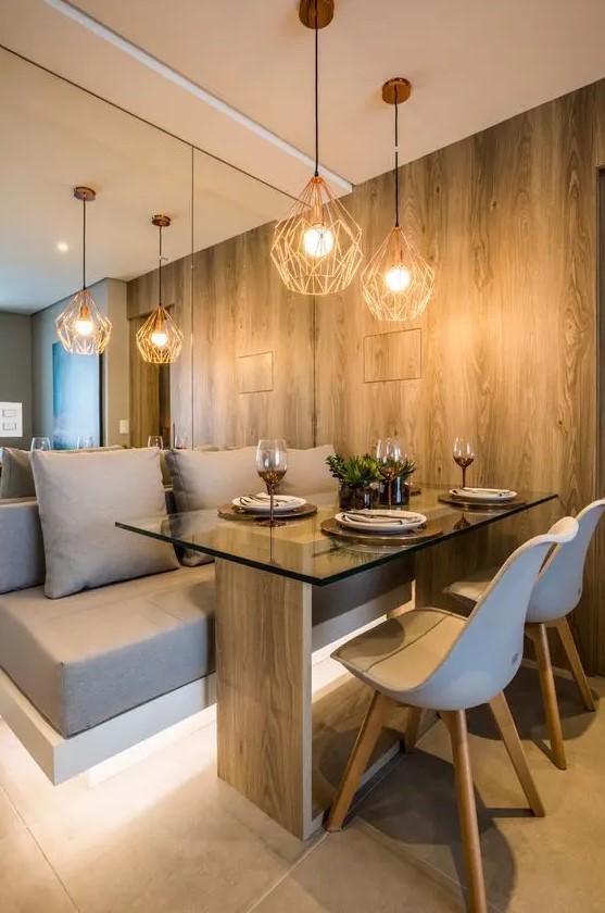 a contemporary dining nook with a mirror wall, a built in and lit up upholstered taupe bench, a wood and glass table and white chairs