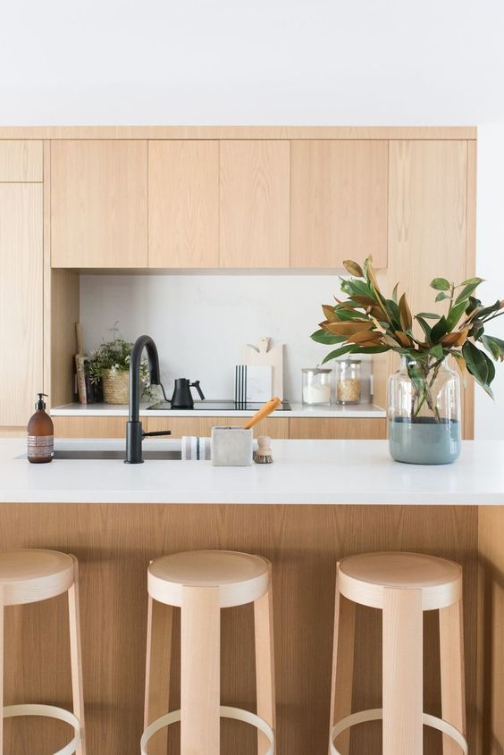 a contemporary light-stained kitchen with no hardware cabinets, a kitchen island with a stone countertop and black fixtures