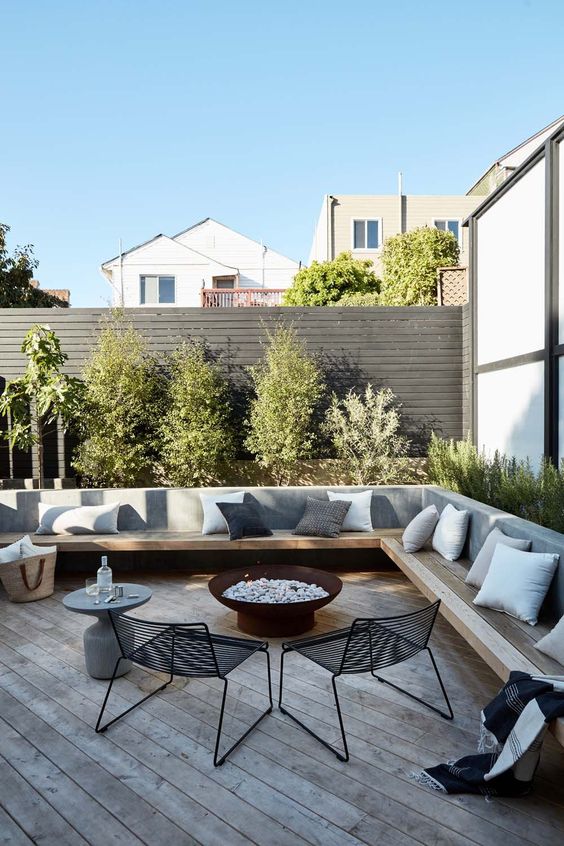 a contemporary terrace with a wooden deck, a floating corner bench with pillows, a fire bowl and metal chairs looks cool