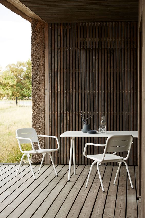 a contemporary terrace with a wooden deck and a roof clad with wooden slats, white metal dining furniture for a contrast