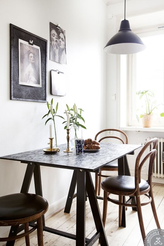 a cool Scandinavian dining space with a trestle and black chairs, a black and white gallery wall and a black pendant lamp