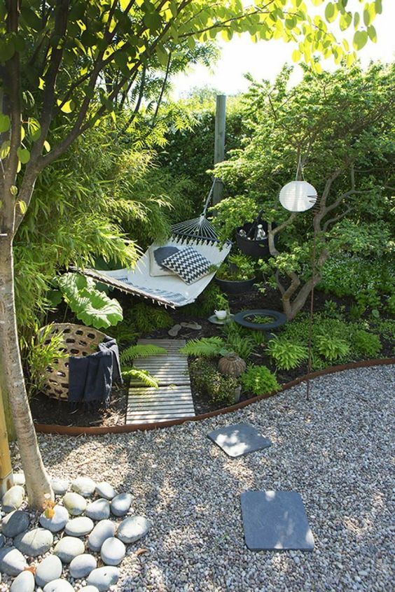 a cool garden nook with lots of greenery, a hammock with pillows, a gravel path with metal edging, a basket with blankets