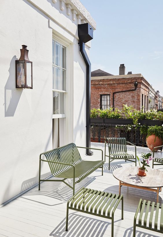 a cool modern terrace with green metal furniture, a round wooden table, greenery and blooms is a lovely space