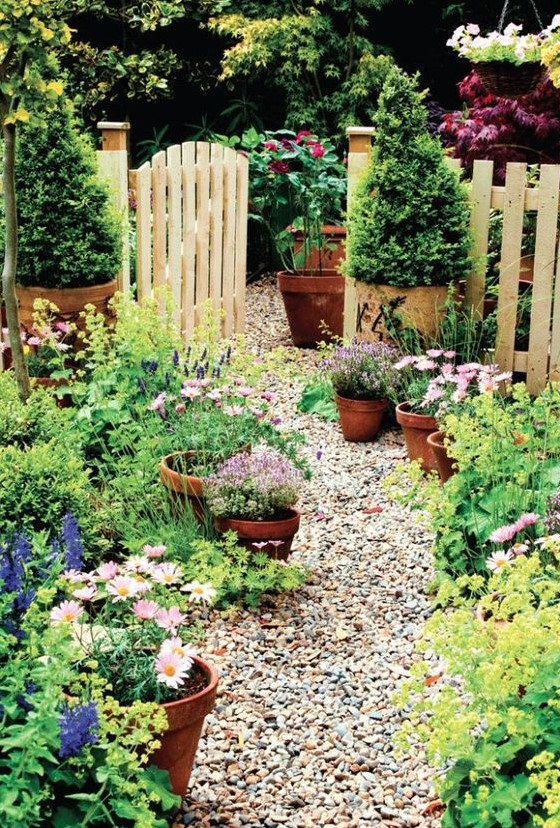 a cozy front yard with a gravel pathway and potted blooms and greenery that line up the path