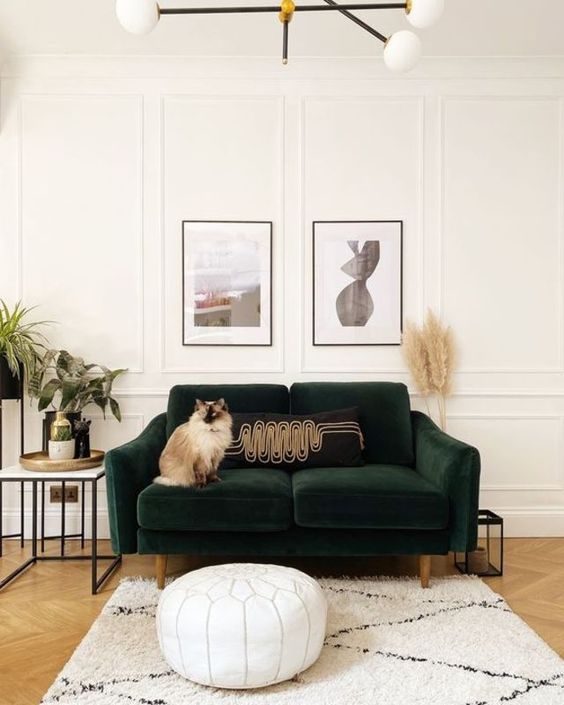 a cute living room done in neutrals, with a dark green sofa, a white leather pouf, a side table, a mini gallery wall