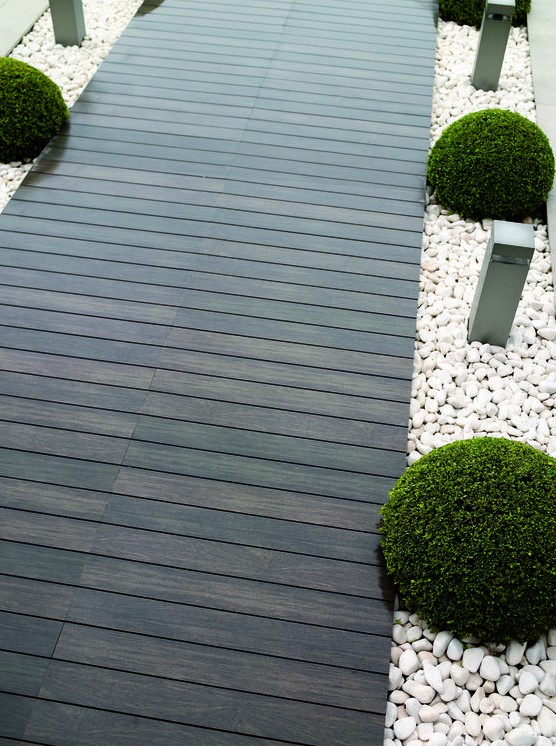 a dark stained wooden path contrasts white pebbles lining and boxwood looks ultra-modern and bold