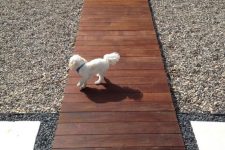 a dark-stained wooden walkway is a chic and stylish idea for a modern outdoor space, gravel around adds texture to the space
